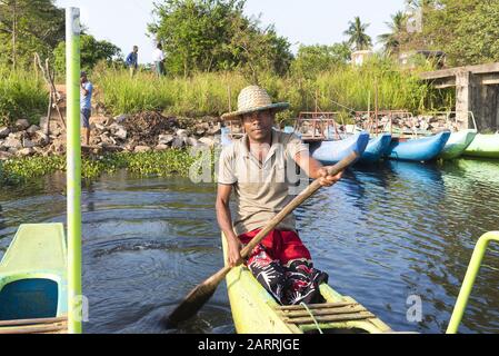 Habrana, Sri Lanka: 03/16/2019: Locale uomo dello Sri Lanka remando barca turistica su un lago. Indossa un tradizionale cappello di paglia. Foto Stock