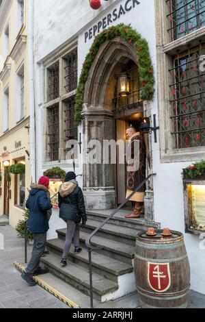 Uomo in abiti tradizionali guardando come due patroni entrare nel ristorante attraverso medievale porta ad arco. Tallinn, Estonia Foto Stock