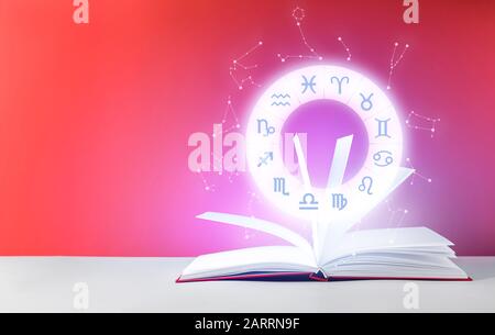 Segni astrologici e libro aperto sul tavolo sullo sfondo a colori Foto Stock