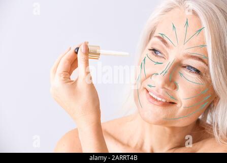 Donna matura con frecce per massaggiare sul viso applicando siero su sfondo chiaro Foto Stock