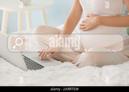 Donna incinta con laptop utilizzando il motore di ricerca web a casa, primo piano Foto Stock