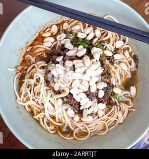 Vista ravvicinata del piatto con noodle in stile Sichuan come spaghetti speziati con ventriglio di pollo, tritato, verdure e arachidi, cucina cinese Foto Stock