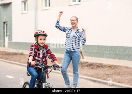 Madre orgogliosa di sua figlia che ha imparato a guidare la bicicletta all'aperto Foto Stock