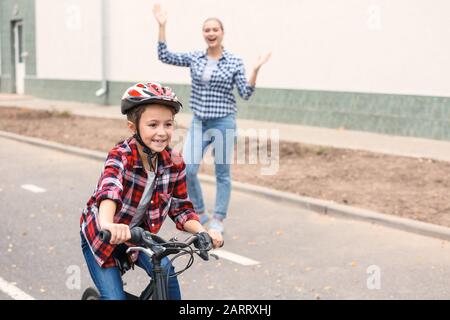 Madre orgogliosa di sua figlia che ha imparato a guidare la bicicletta all'aperto Foto Stock