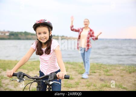 Madre orgogliosa di sua figlia che ha imparato a guidare la bicicletta all'aperto Foto Stock