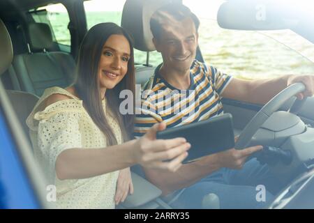Felice coppia prendere selfie nella loro nuova auto, vista dal parabrezza Foto Stock