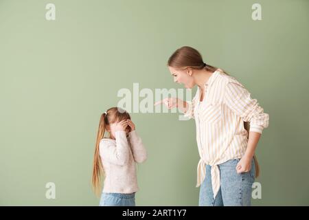 Madre arrabbiata scolando sua figlia piccola su sfondo colore Foto Stock