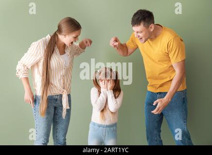 Genitori arrabbiati che scolano la loro figlia piccola sullo sfondo di colore Foto Stock