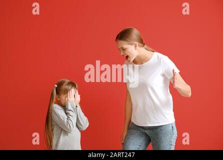 Madre arrabbiata scolando sua figlia piccola su sfondo colore Foto Stock