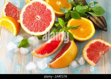 Ingredienti per preparare una bevanda rinfrescante. Pompelmo, arancia, ghiaccio e basilico su un tavolo di legno. Foto Stock