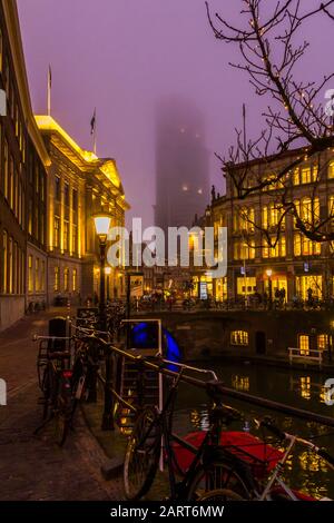 Utrecht, Paesi Bassi, 21st Gennaio 2020. Un ponte di pietra ad arco attraverso il canale nel centro di Utrecht. Serata Misty, vista notturna del canale, Torre Dom Foto Stock
