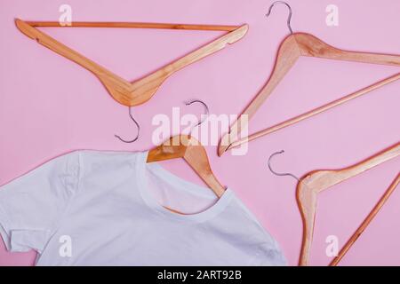 Maglietta bianca e grucce in legno su sfondo rosa pastello Foto Stock