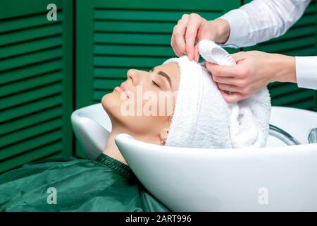 Parrucchiere che avvolge i capelli della donna in asciugamano dopo aver lavato la testa nel salone di bellezza, primo piano. Foto Stock