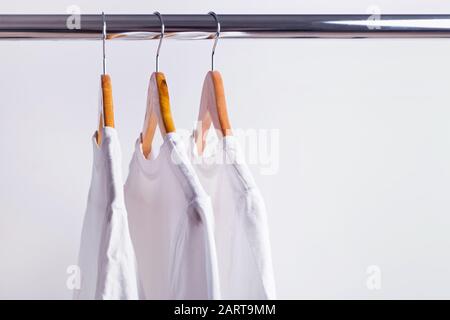 Tre t-shirt in wite appese su appendiabiti in legno Foto Stock