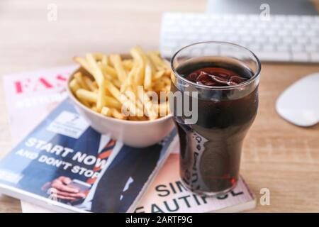 Bicchiere di cola fredda con patatine fritte e riviste su tavola di legno Foto Stock