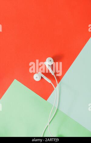 coppia di cuffie auricolari su sfondo colorato e luminoso. Vista dall'alto di una cuffia cablata su sfondo rosso e verde Foto Stock