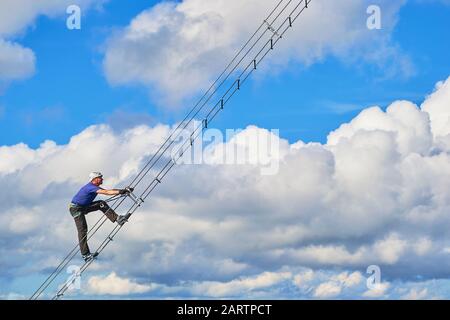 Guy su via ferrata Intersport, Donnerkogel montagne, vicino a Gosau, Austria. Sezione astratta di una scala diagonale contro nuvole bianche e cielo blu - s. Foto Stock