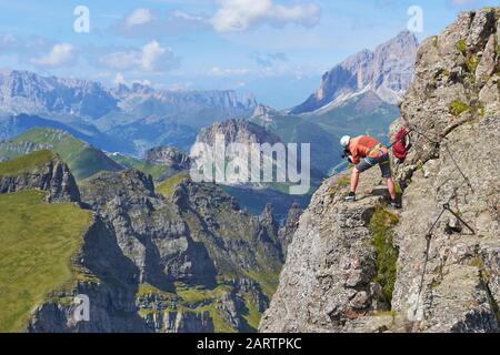 Uomo che scatta foto assicurato ad un cavo via ferrata, alto su delle Trincee klettersteig, nelle montagne delle Dolomiti, durante una luminosa giornata estiva con Foto Stock