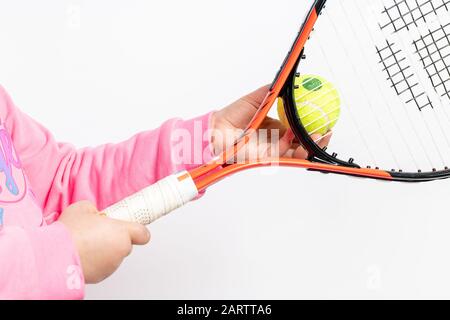 La ragazza che indossa una felpa rosa tiene la racchetta da tennis e la palla da tennis su sfondo bianco Foto Stock