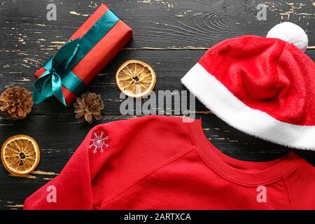 Vestiti di Natale con scatola regalo e cappello di Babbo Natale su sfondo di legno Foto Stock