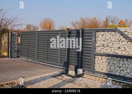 Cancello d'ingresso automatico utilizzato in combinazione con una parete di gabione. Foto Stock