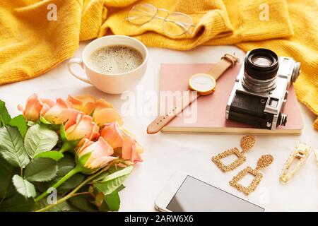 Fiori di rosa con fotocamera, tazza di caffè, telefono cellulare e accessori femminili su sfondo bianco Foto Stock
