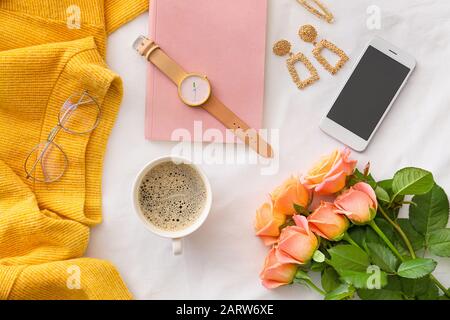Fiori di rosa con telefono cellulare, tazza di caffè e accessori femminili su sfondo bianco Foto Stock