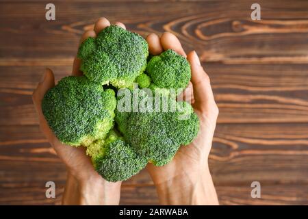 Mani femminili con cavolo fresco di broccoli su sfondo di legno, vista dall'alto Foto Stock