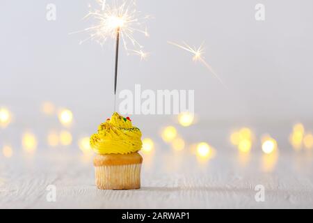 Gustoso cupcake con sparkler su tavolo bianco con luci sfocate Foto Stock