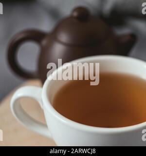 Tazza di tè in porcellana bianca e teapot in argilla marrone scuro su un cuore in legno tagliato a laser sul copriletto grigio Foto Stock