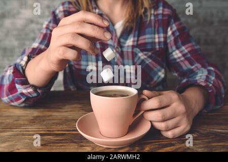 Donna che rilascia i cubetti di zucchero in tazza con caffè caldo a tavola, primo piano Foto Stock