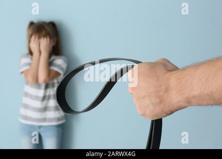 Uomo che minaccia la sua figlia piccola contro sfondo di colore. Concetto di punizione fisica Foto Stock