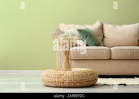 Vaso con guglie di grano sul pouf in vimini in camera Foto Stock