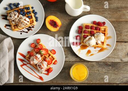 Piatti con gustosi waffle, frutti di bosco e gelato a tavola Foto Stock