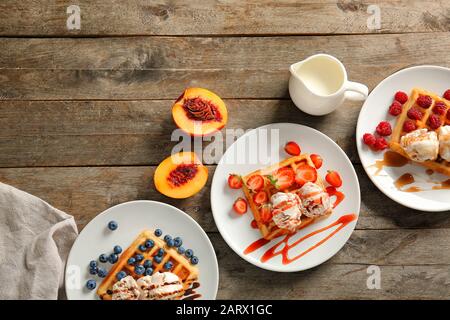Piatti con gustosi waffle, frutti di bosco e gelato a tavola Foto Stock