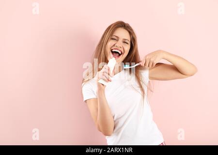 Giovane donna che usa il tubo di pasta dentale come microfono su sfondo a colori Foto Stock