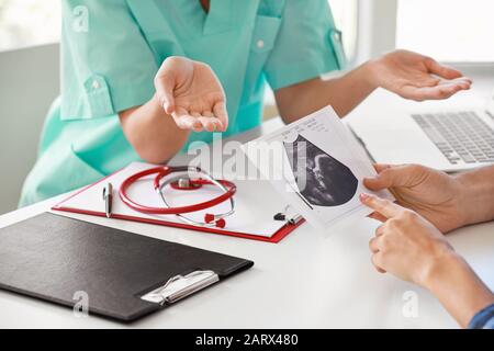 Ginecologo femminile che mostra una scansione ecografica di coppia in clinica, closeup Foto Stock