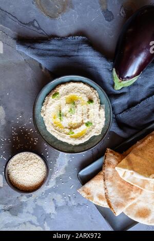 Delizioso bagno di melanzane Baba Ganoush condito con semi di sesamo e olio d'oliva, servito con pane pita su sfondo rustico Foto Stock