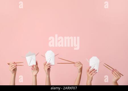 Molte mani con contenitori per cibo asiatico e bacchette su sfondo a colori Foto Stock