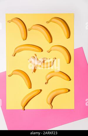 Banana sbucciata tra quelli non sbucciati su sfondo colorato. Concetto di unicità Foto Stock