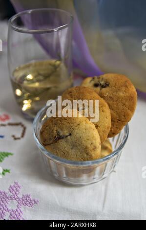 Biscotti fatti in casa in una tazza di vetro e un bicchiere con un'infusione di erbe su una stuoia bianca Foto Stock