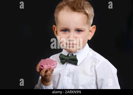 Ritratto di pianto ragazzino con dolce meringa su sfondo scuro Foto Stock