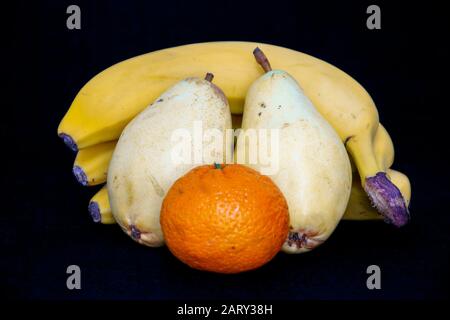 Ree banane, due pere e una mandarino su sfondo nero, Frutta, insalata, colazione, dessert, fetta di cibo Foto Stock