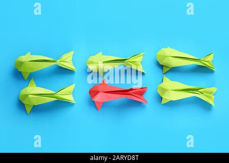 Pesce origami rosso tra quelli verdi su sfondo colorato. Concetto di unicità Foto Stock