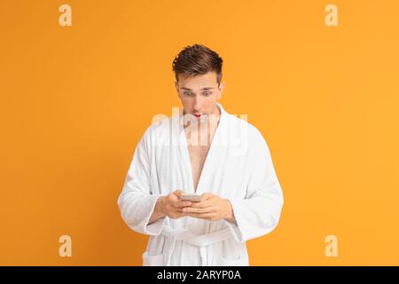 Uomo scioccato in accappatoio e con telefono cellulare su sfondo a colori Foto Stock