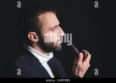 Ritratto di un giovane elegante con tubo fumante su sfondo scuro Foto Stock