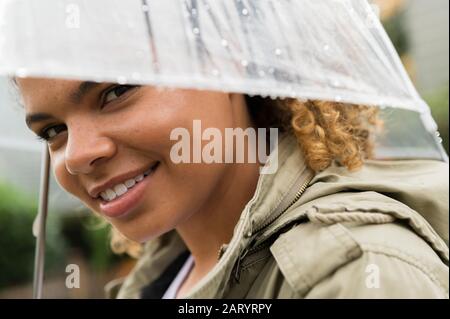 Donna sorridente sotto ombrello bagnato Foto Stock