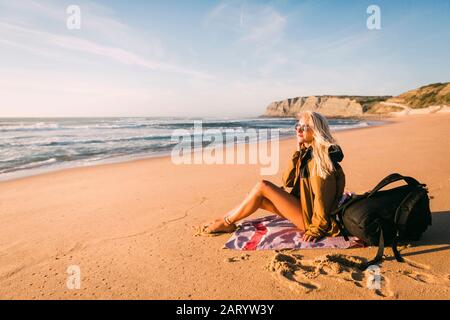 Donna seduta su asciugamano sulla spiaggia Foto Stock