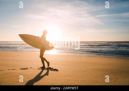 Donna che tiene la tavola da surf contro la luce del sole sulla spiaggia Foto Stock