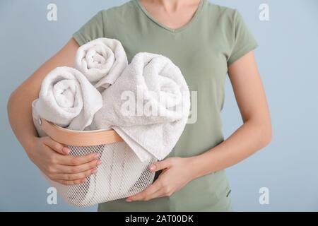 Donna che tiene il cesto con gli asciugamani puliti sullo sfondo di colore Foto Stock